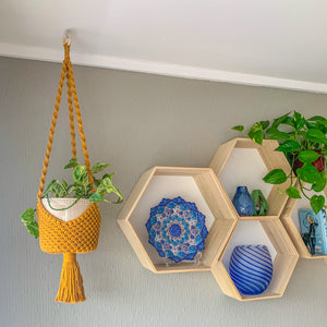 A yellow basket-style macrame plant hanger with a pothos hanging plant in a white planter hanging from the ceiling.