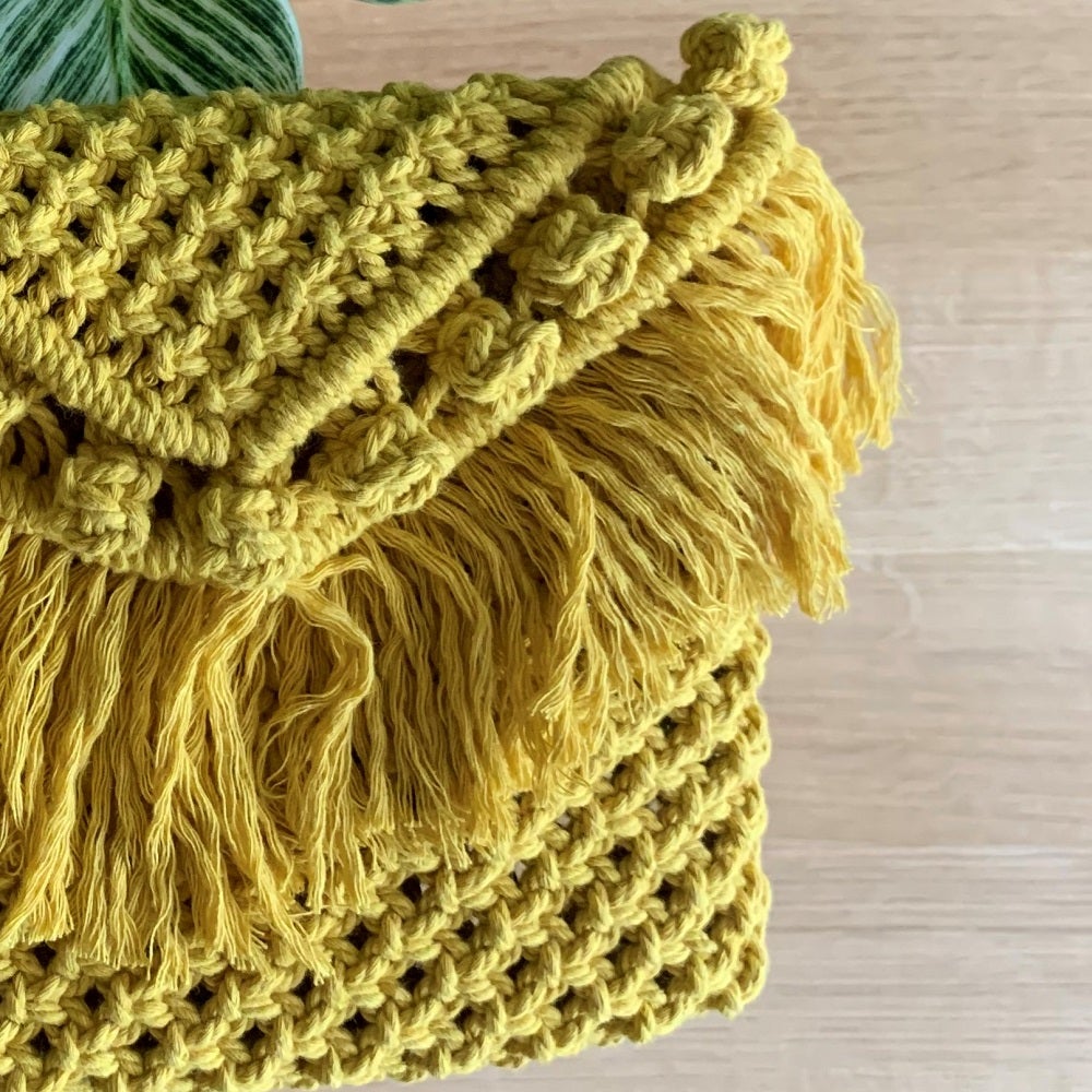 A yellow handcrafted macrame clutch bag on a table with an indoor plant on it 