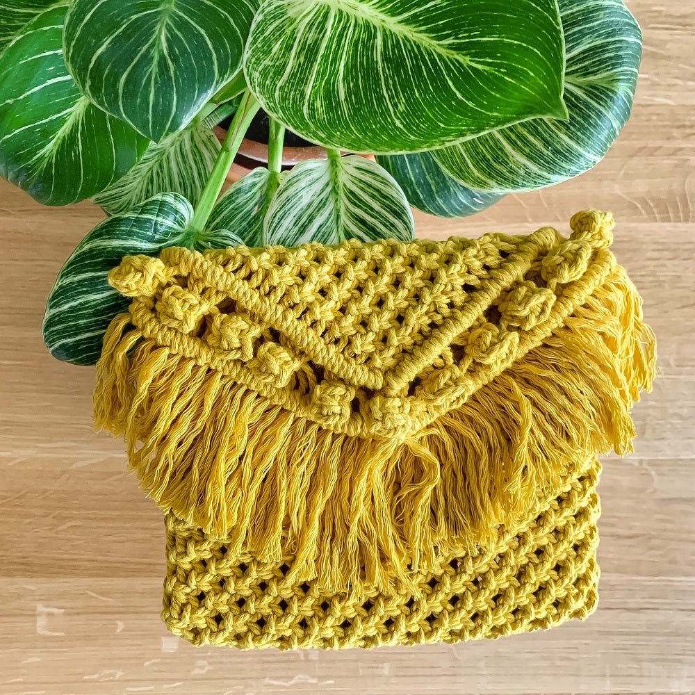 A yellow handcrafted woven clutch bag on a table with an indoor plant on it 