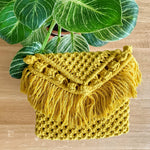Load image into Gallery viewer, A yellow handcrafted woven clutch bag on a table with an indoor plant on it 
