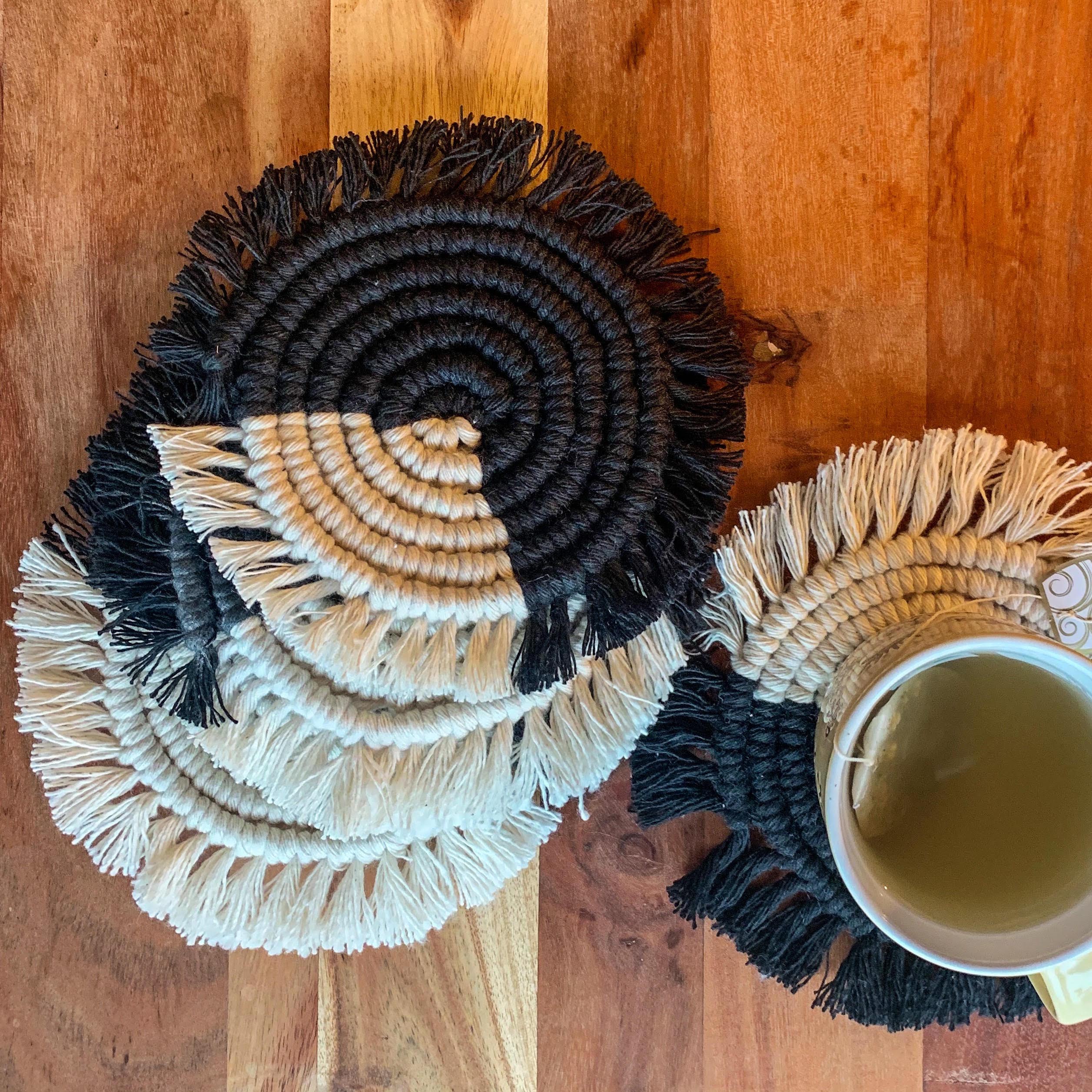 A cup of tea placed on a round handwoven coaster. This is a set of 4 round macrame coasters made with black and white cotton yarn.