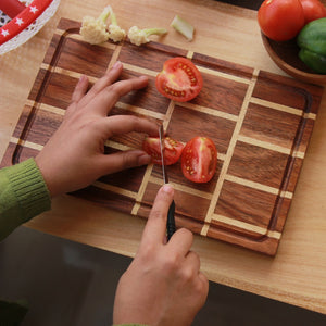 A tomato being cut on a brick pattern wooden cutting board made from Walnut and Birch Wood. 