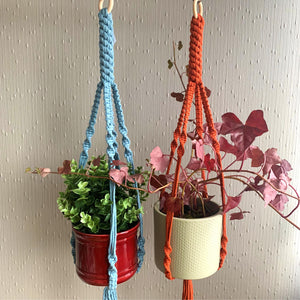 A blue and a orange macrame plant hanger with indoor plants in a maroon pot and a green planter hanging from the ceiling