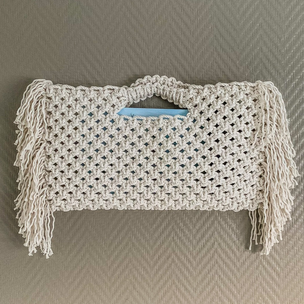 A white bohemian beach bag with fringe detailing hanging on a wall