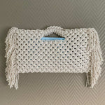 Load image into Gallery viewer, A white bohemian beach bag with fringe detailing hanging on a wall
