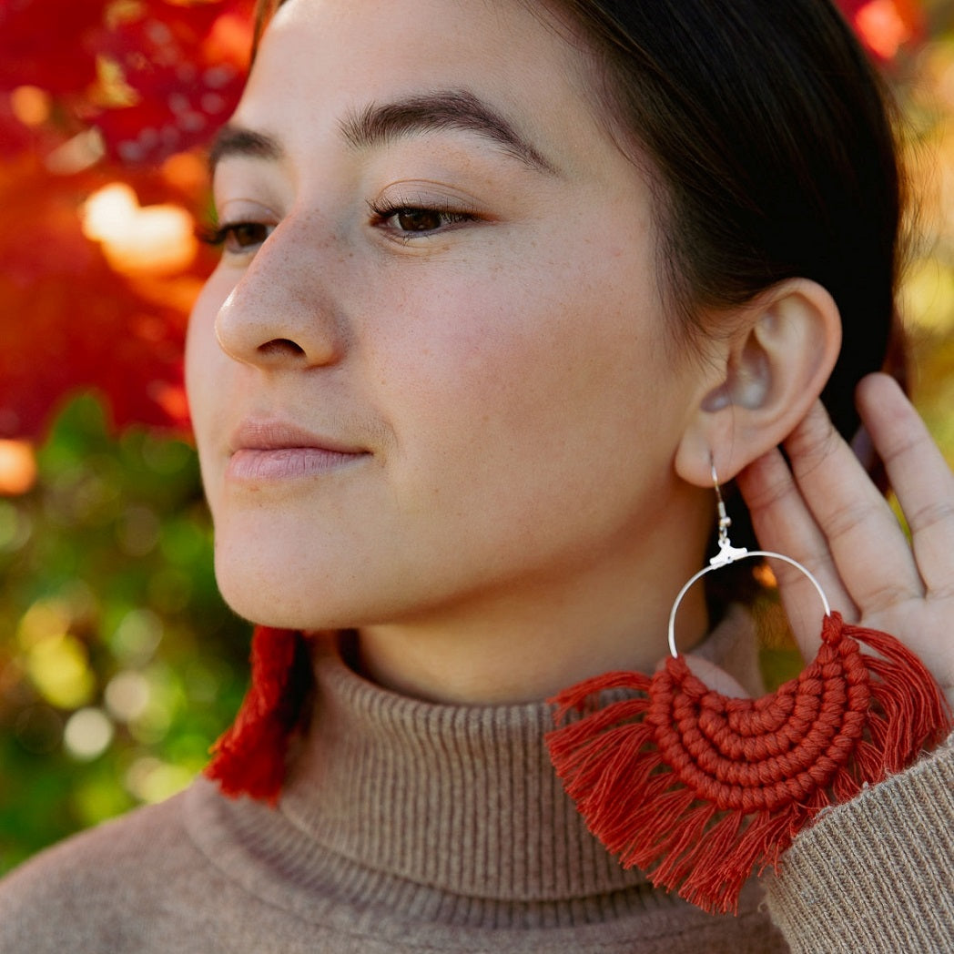 A woman wearing a fringed boho earrings that is handmade with cotton yarn in burnt orange.