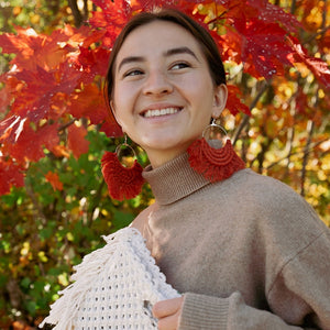 A woman wearing a fringed boho earrings that is handmade with cotton yarn in burnt orange.