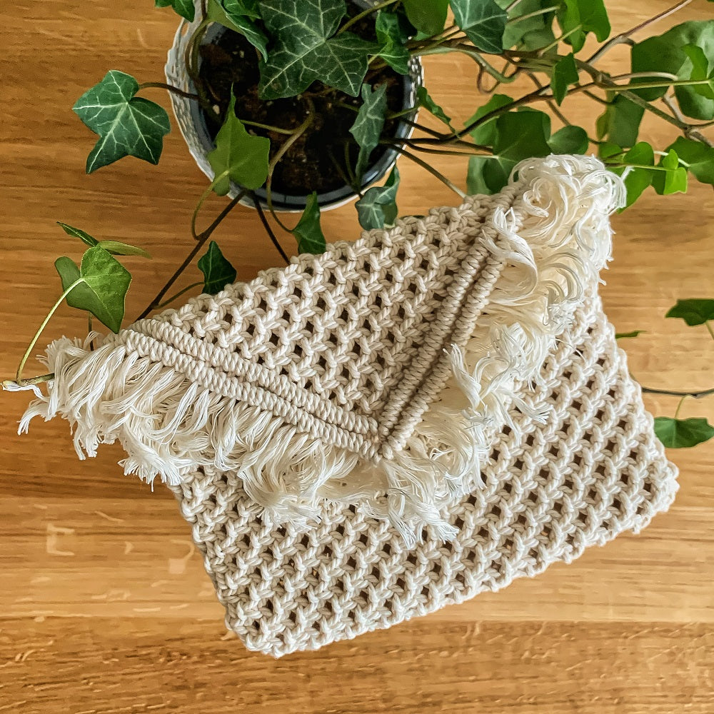 A white macrame envelope clutch bag on a table with an ivy plant