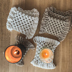 Load image into Gallery viewer, A set of 4 white and 4 beige macrame coasters with two candles on coasters used as candle mats.
