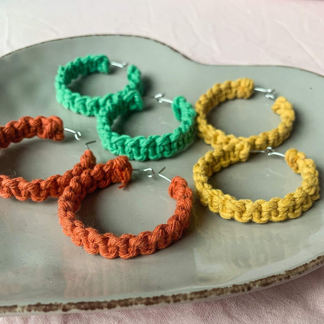 Three pairs of macrame hoop earrings on a tray in the colour green, orange and yellow.