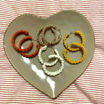 Load image into Gallery viewer, Four pairs of macrame hoop earrings on a heart shaped tray in the colours rose gold, orange, white and yellow.
