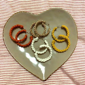 Four pairs of macrame hoop earrings on a heart shaped tray in the colours rose gold, orange, white and yellow.