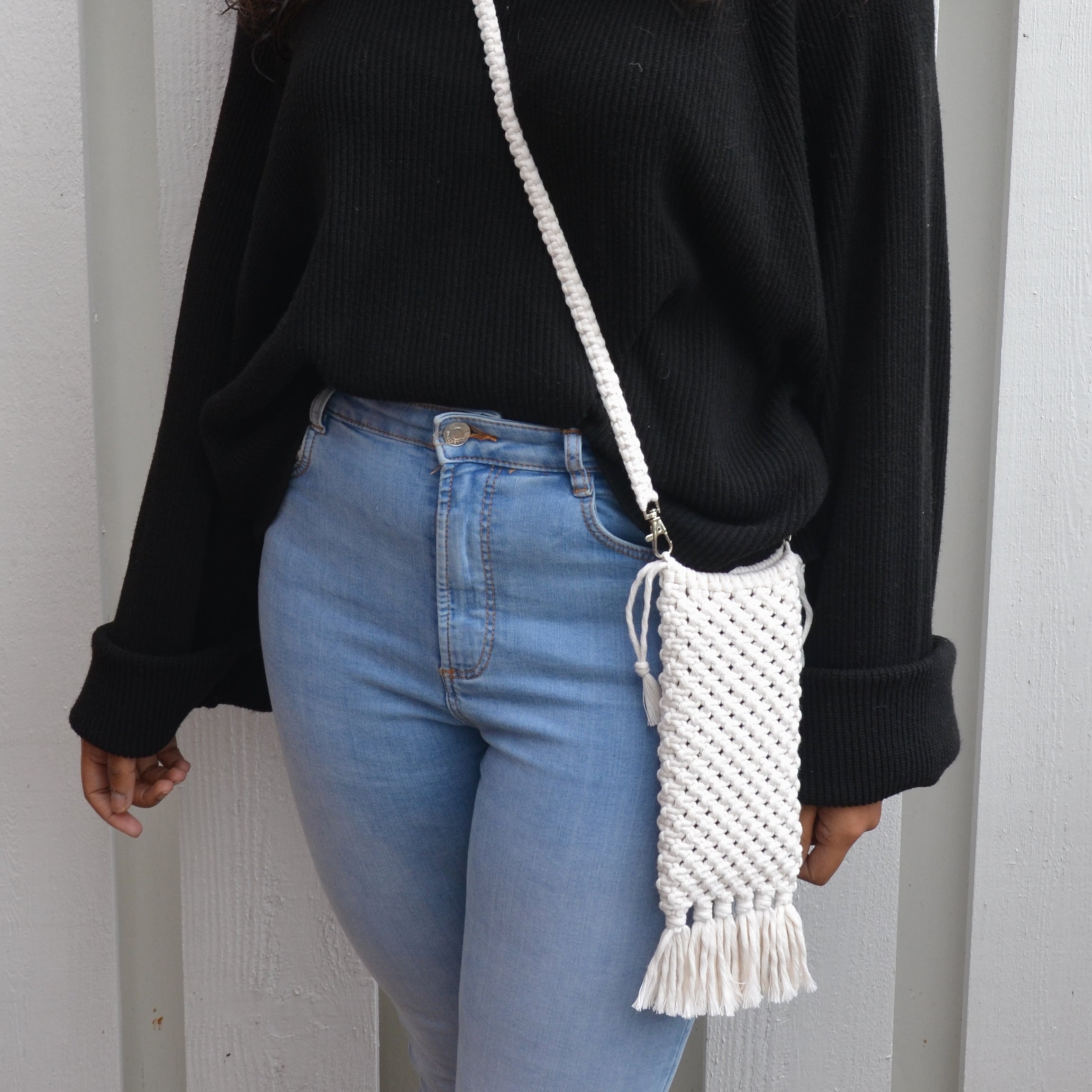 A woman carrying a white crossbody macrame bag with fringe detailing and a shoulder strap