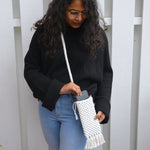 Load image into Gallery viewer, A woman putting her phone into a white macrame mobile phone bag with fringe detailing
