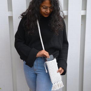 A woman putting her phone into a white macrame mobile phone bag with fringe detailing