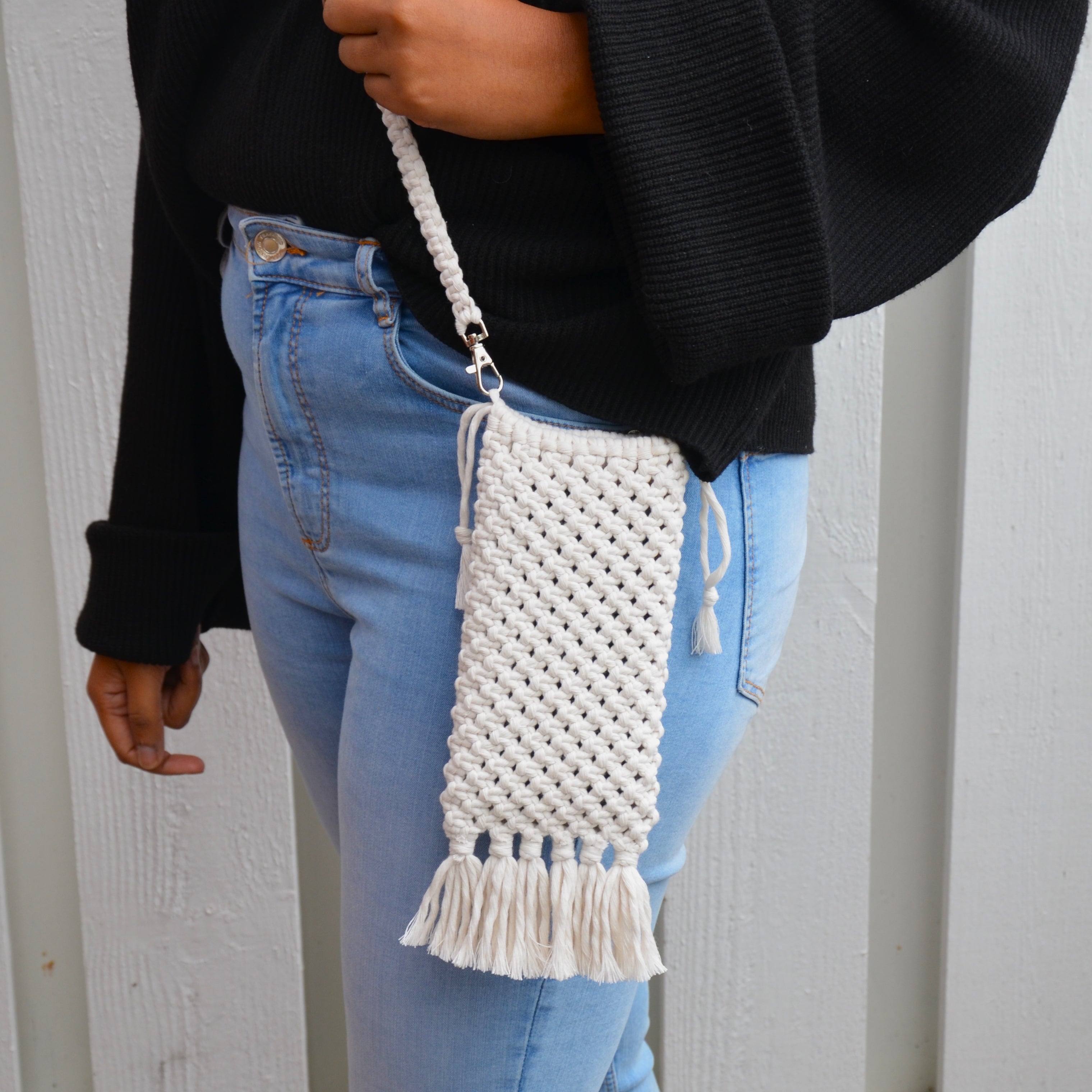 A woman carrying a white macrame mobile phone bag with fringe detailing and a shoulder strap