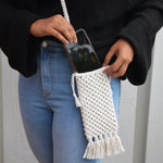 Load image into Gallery viewer, A woman putting her phone into a white macrame mobile phone bag with fringe detailing

