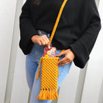 Load image into Gallery viewer, A woman putting her phone into a mustard yellow woven mobile phone bag with fringe detailing and a shoulder strap
