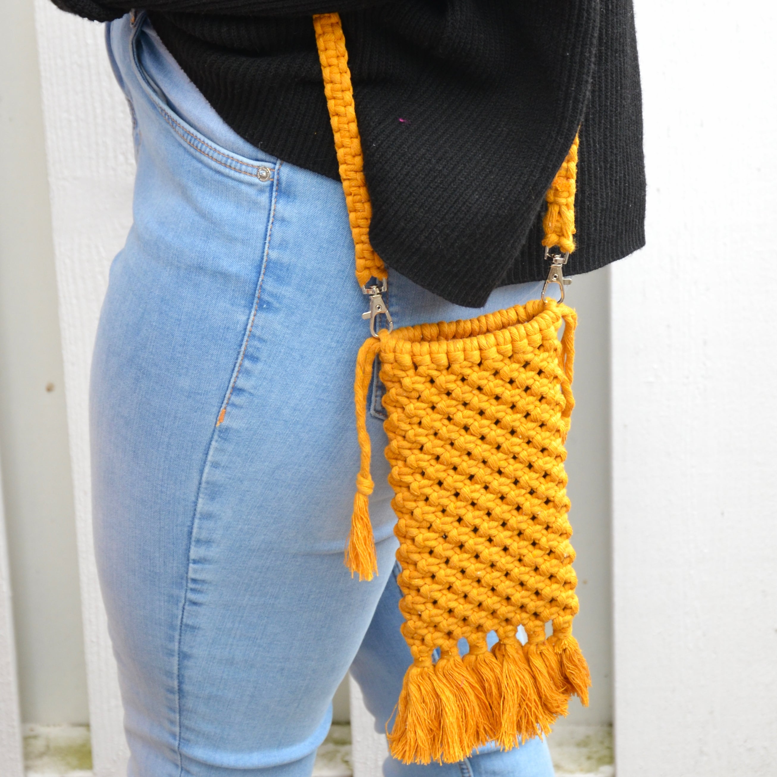 A woman carrying a mustard yellow macrame mobile phone bag with fringe detailing and a shoulder strap