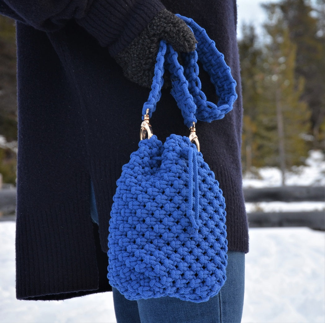 A woman carrying a royal blue woven bucket bag with drawstring closure and a shoulder strap