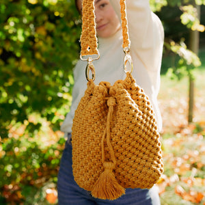 A woman carrying a mustard yellow woven bucket bag with drawstring closure and a shoulder strap