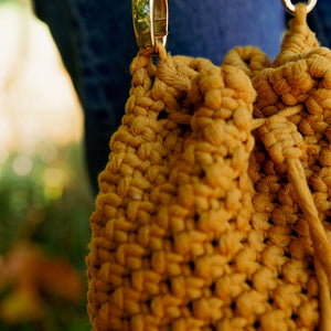 Macrame knot detailing on a mustard yellow macrame bucket bag with draw string closure