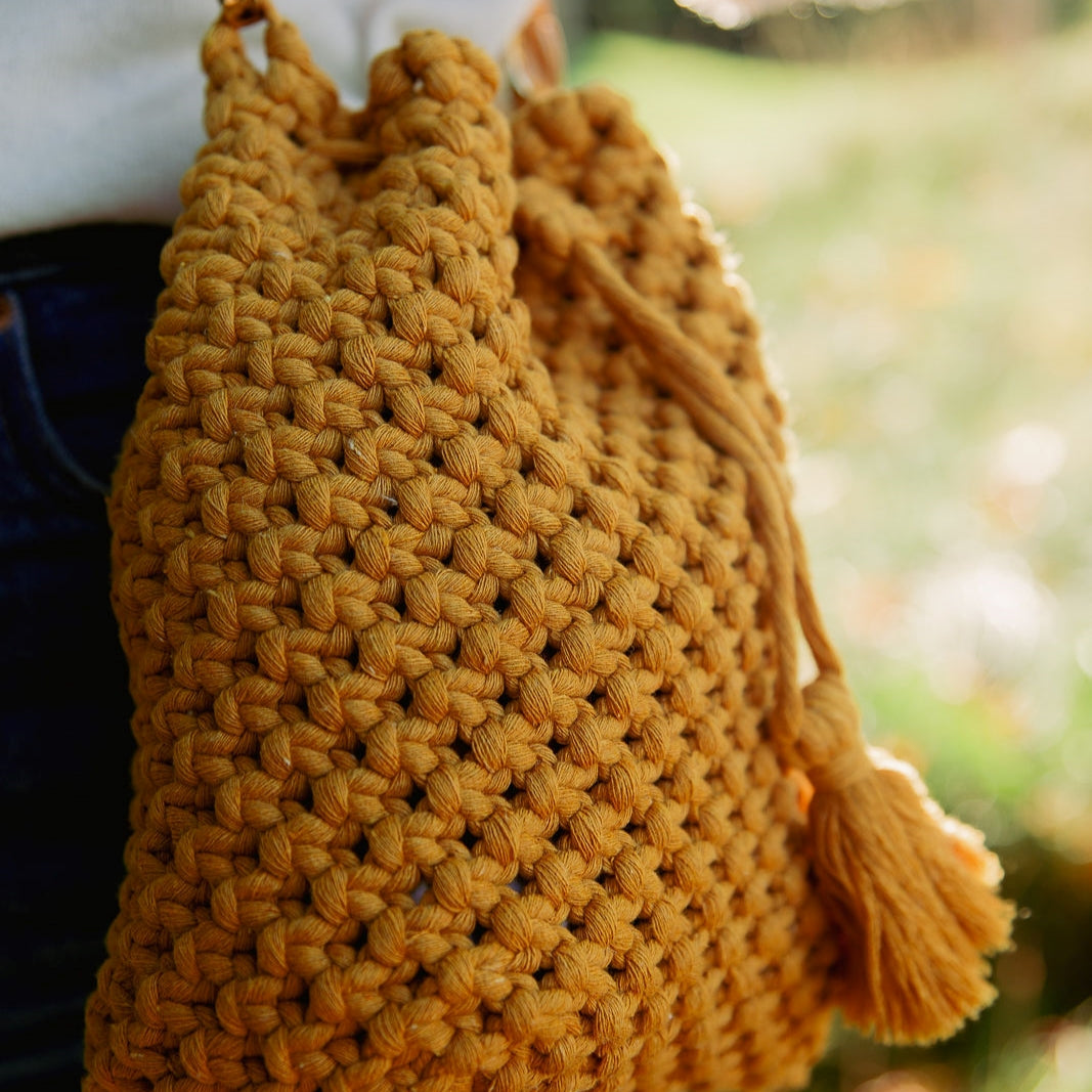 A close-up shot of macrame knots on a mustard yellow handcrafted bucket bag with a tassel