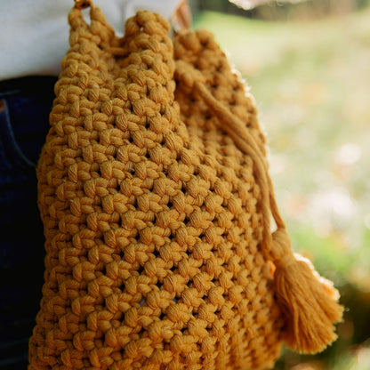 A close-up shot of macrame knots on a mustard yellow handcrafted bucket bag with a tassel