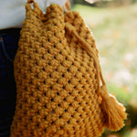 Load image into Gallery viewer, A close-up shot of macrame knots on a mustard yellow handcrafted bucket bag with a tassel
