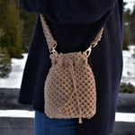 Load image into Gallery viewer, A woman carrying a brown woven bucket bag with drawstring closure and a shoulder strap
