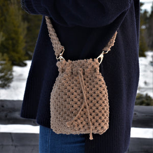 A woman carrying a brown woven bucket bag with drawstring closure and a shoulder strap