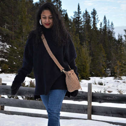 A woman carrying a brown macrame crossbody bucket bag with drawstring closure and a shoulder strap