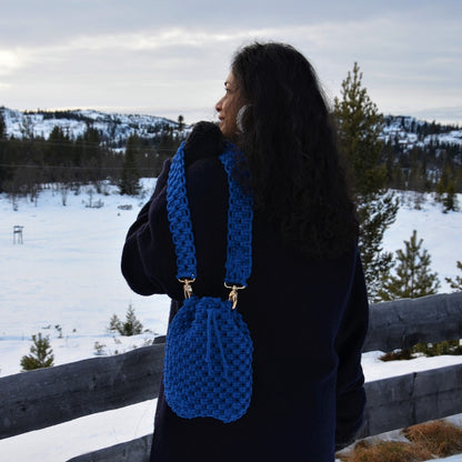 A woman carrying a royal blue woven bucket bag with drawstring closure and a shoulder strap