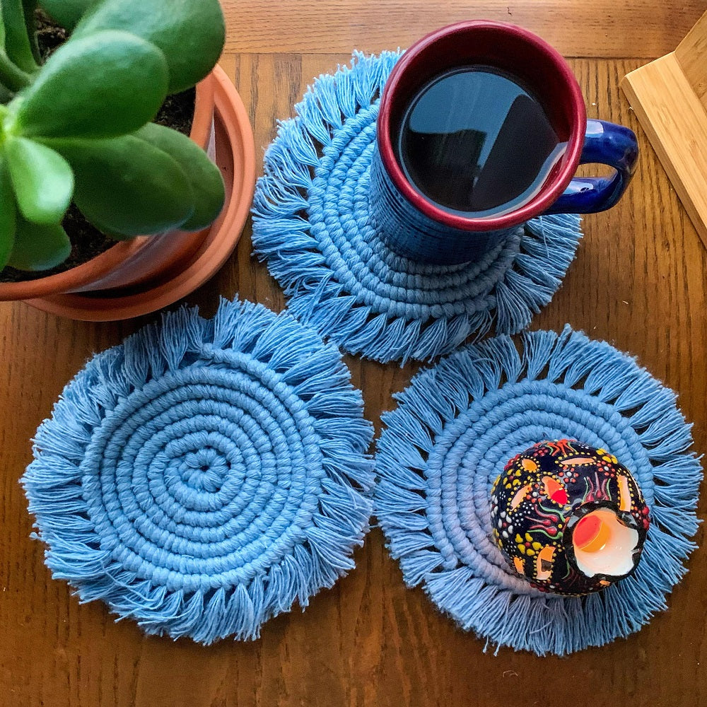 3 macrame round tea coasters with a cup of tea and a small vase on it.