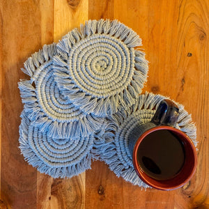 A set of four macrame drink coasters with a cup of tea on it.