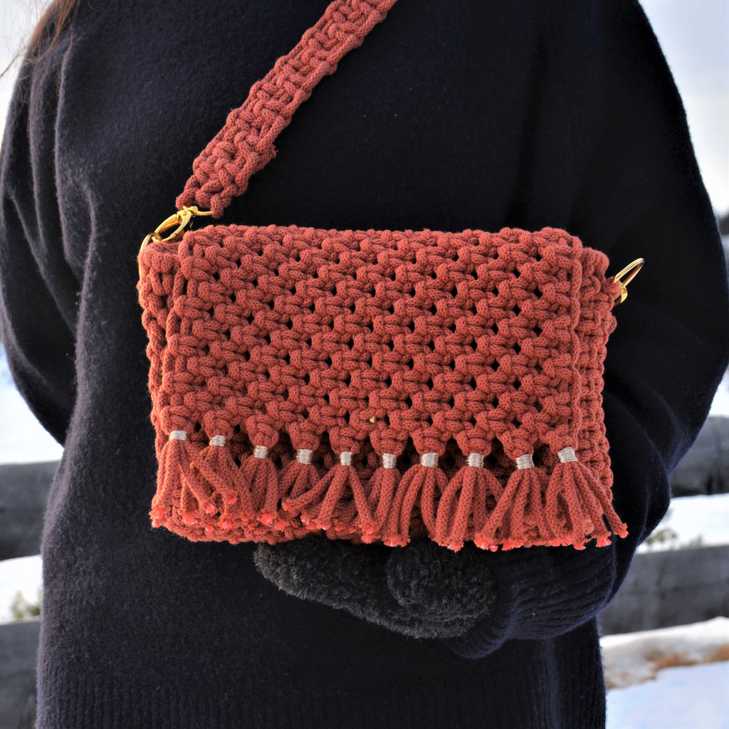 A woman holding a brick coloured woven shoulder bag with a detachable strap