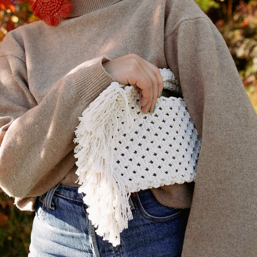 A girl holding a white bohemian macrame bag with fringe detailing