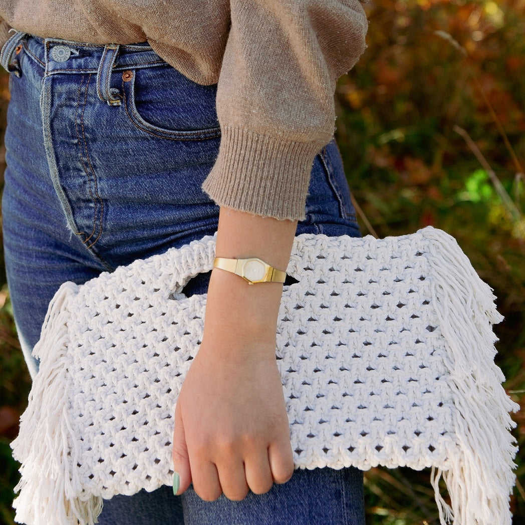 A girl holding a white woven beach bag with fringe detailing