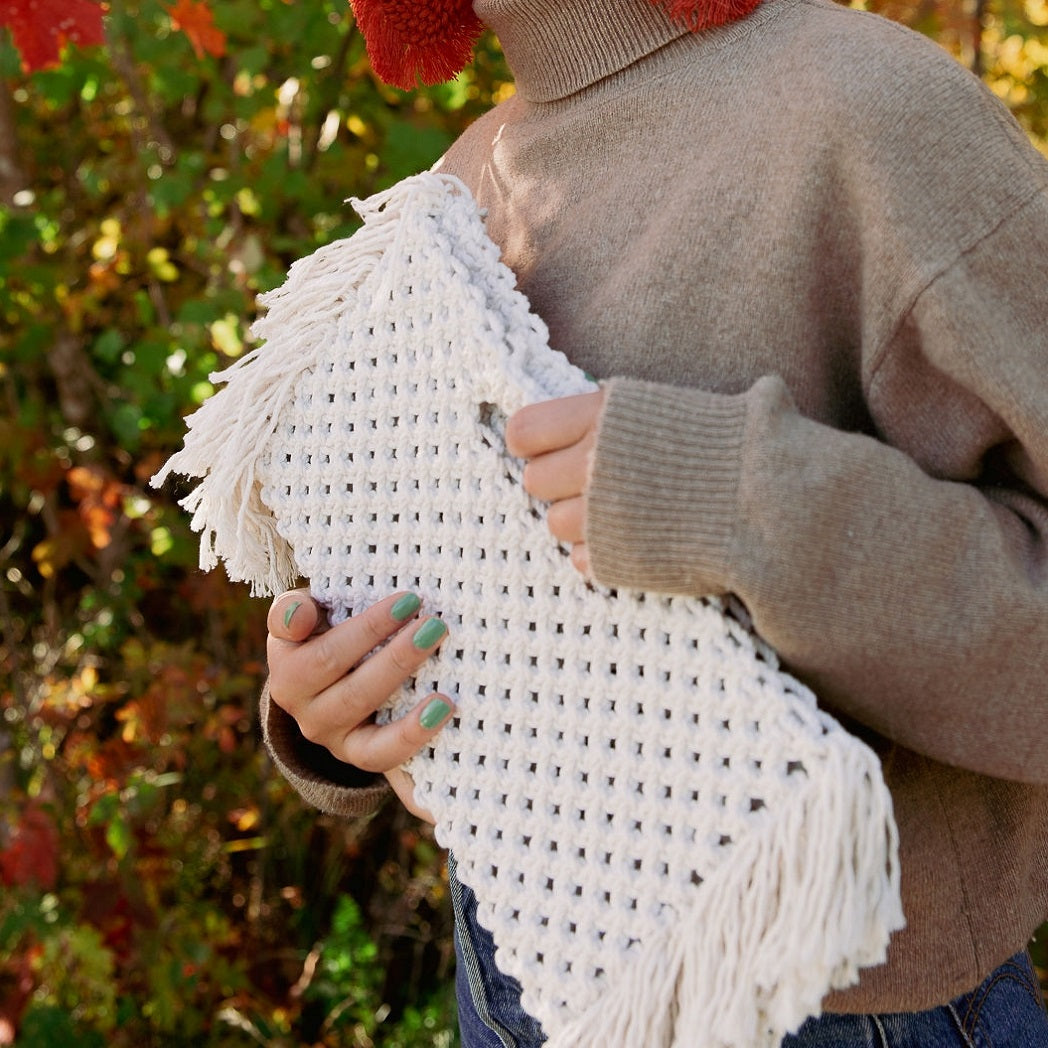 A girl holding a white bohemian macrame bag with fringe detailing