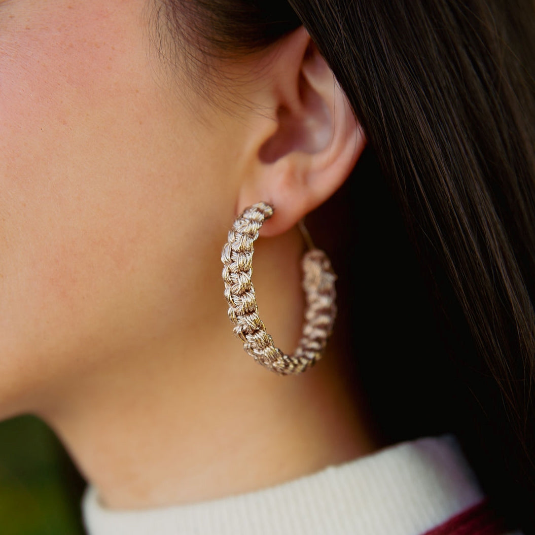 A woman wearing macrame hoop earrings that is handmade with cotton yarn in the colour rose gold.