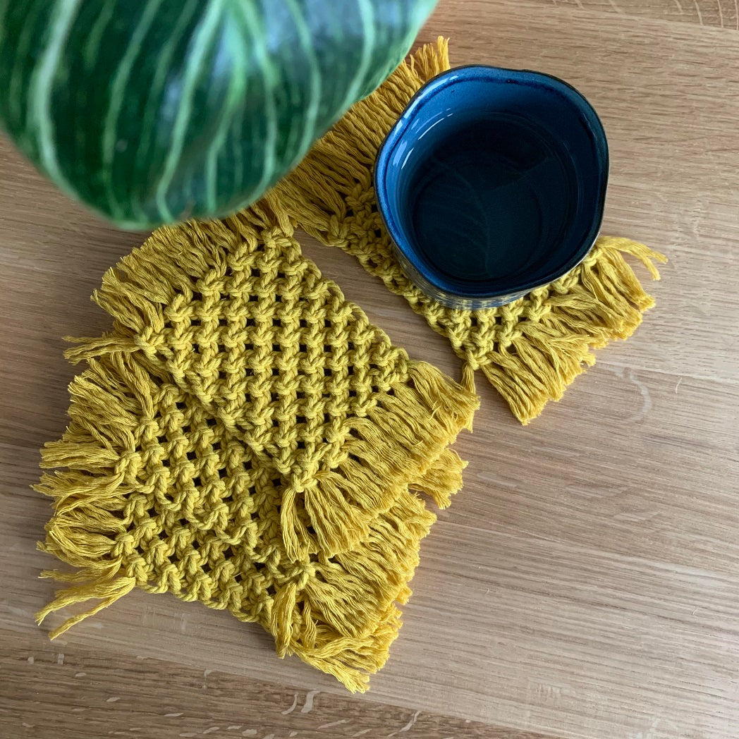 A set of 4 mustard yellow macrame coasters with a cup of tea on a coaster.