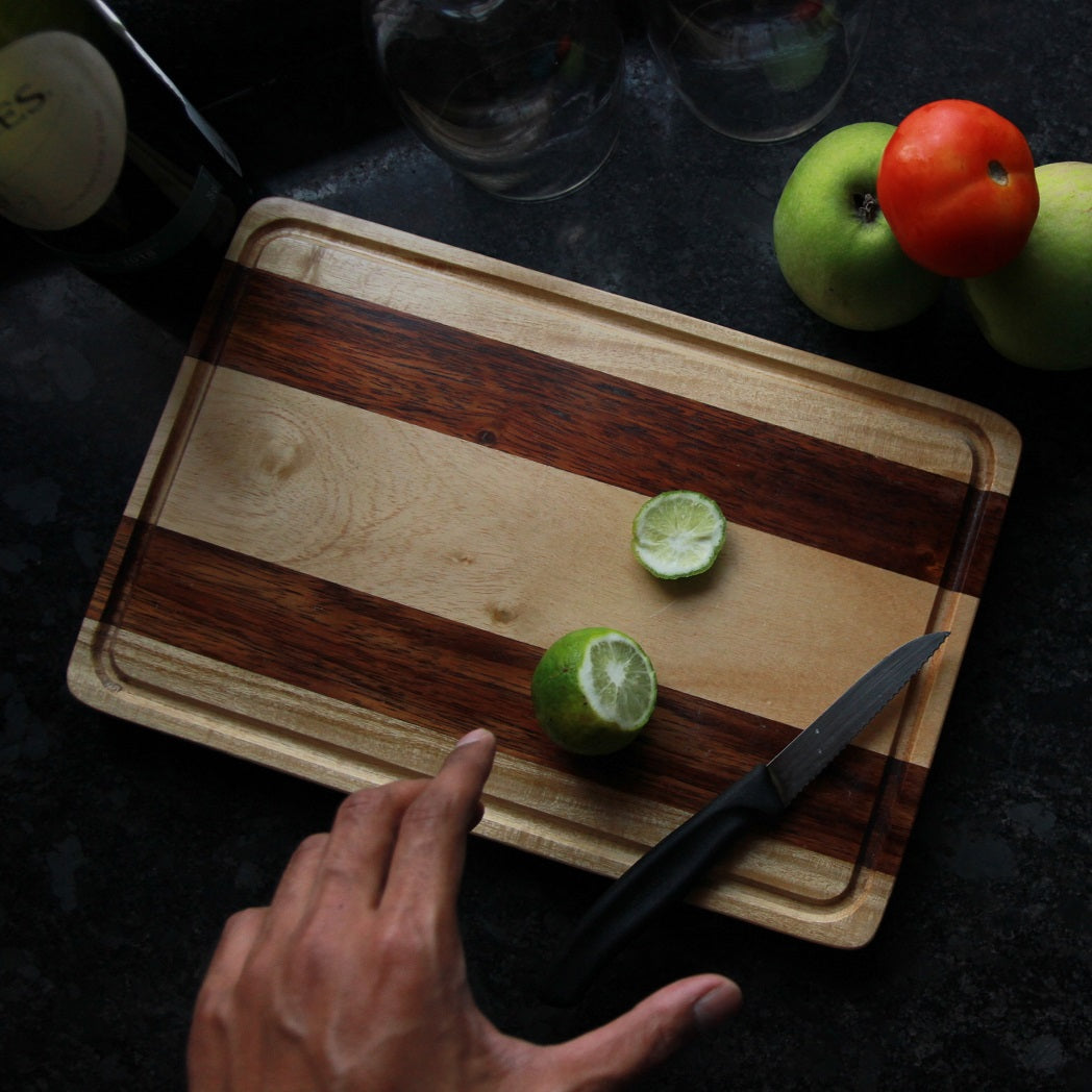 A striped walnut wood and birch wood cutting board with a lemon on it
