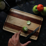 Load image into Gallery viewer, A striped walnut wood and birch wood cutting board with a lemon on it
