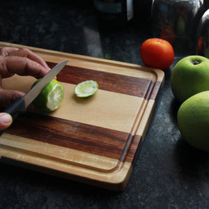 A lemon being cut on a walnut wood and birch wood striped chopping board
