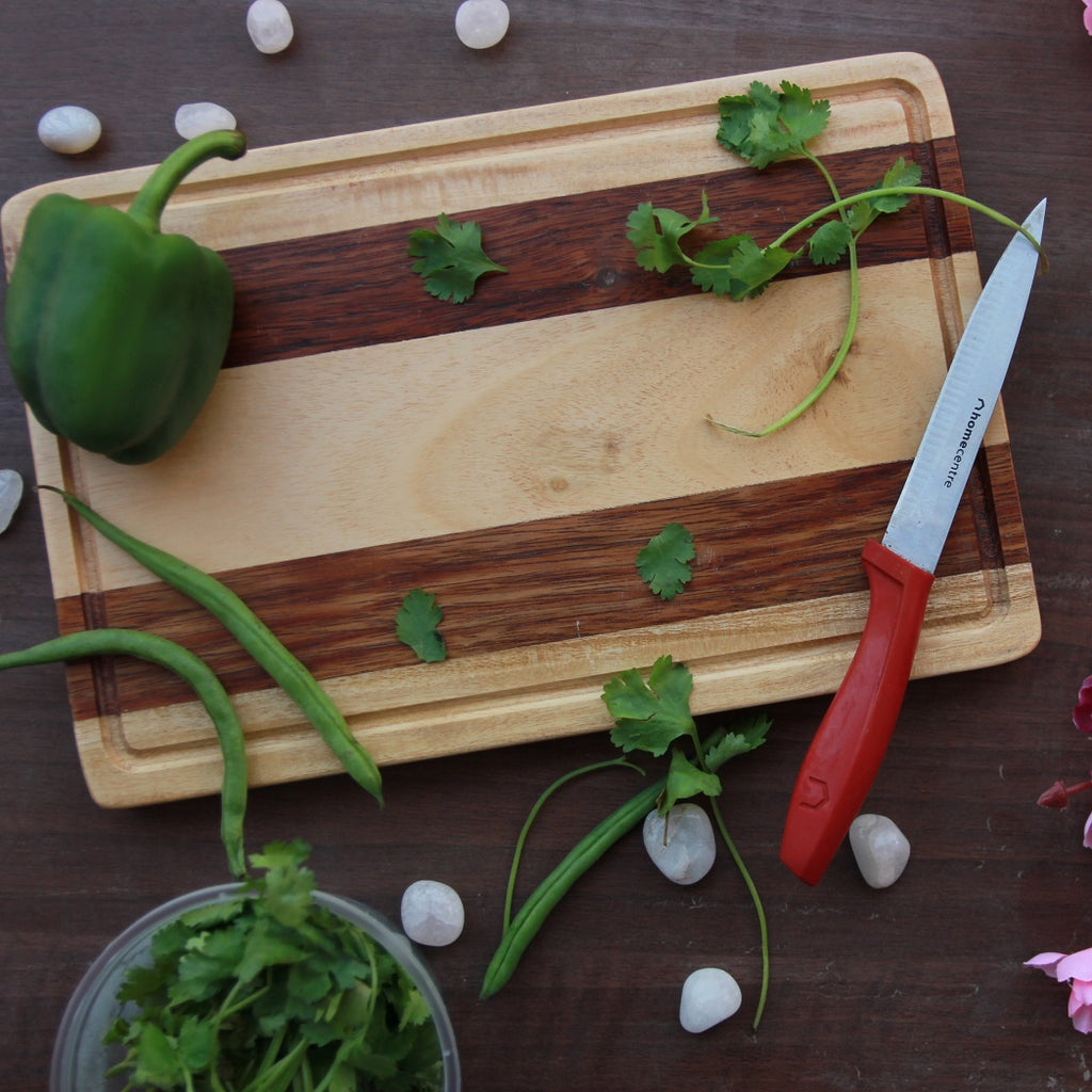 A striped walnut wood and birch wood cutting board with a bell pepper and coriander leaves on it