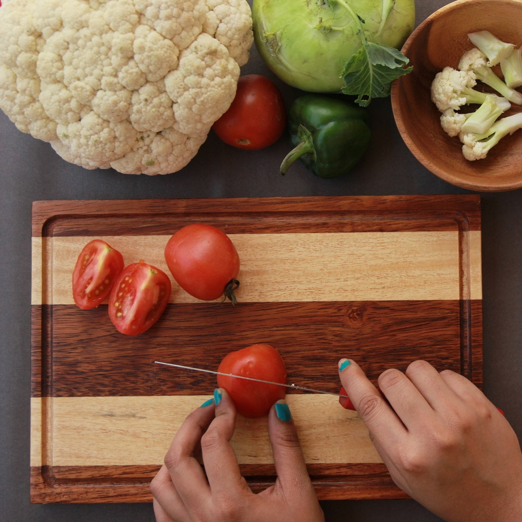 Tomatoes being cut on a walnut wood and birch wood striped chopping board.