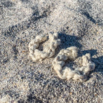 Load image into Gallery viewer, A pair of handmade white macrame hoop earrings on sand.
