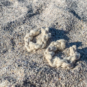 A pair of handmade white macrame hoop earrings on sand.