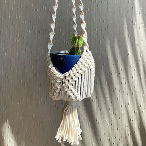 Intricate macrame knots on a white boho basket plant hanger with a green cactus in a blue planter