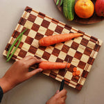 Load image into Gallery viewer, A chessboard style wooden cutting board made with brown walnut and birch wood with carrots being cut on it.
